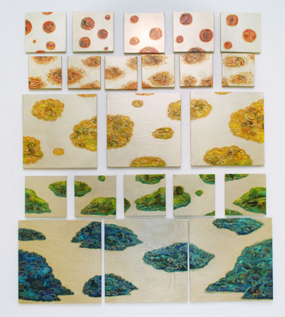 An installation wall of about twenty small white panels, each with red, gold, green or blue island shapes